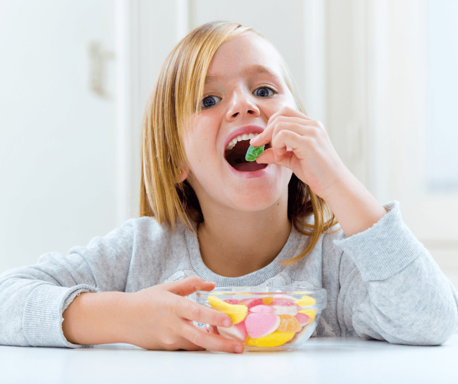 Une jeune fille mangeant des bonbons colorés, mettant en lumière les dangers d’une consommation excessive de sucre chez les enfants.